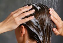 Die perfekte Frisur für die Hochzeit Nahaufnahme einer Frau beim Haarewaschen unter der Dusche, Hände massieren Shampoo-Schaum ins nasse Haar – Symbolfoto für Haarpflege.